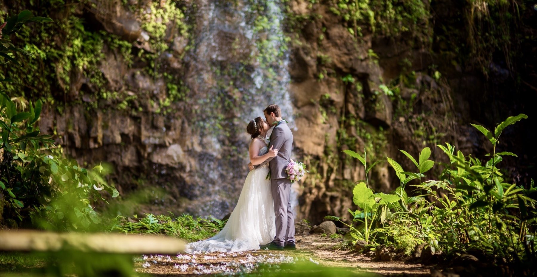 Newlywed couple kissing at the base of a private waterfall on Kauai